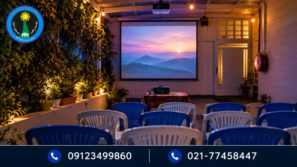 فضای مشترک با پرده نمایش، صندلیهای آبی و سفید، گیاهان و نور گرم